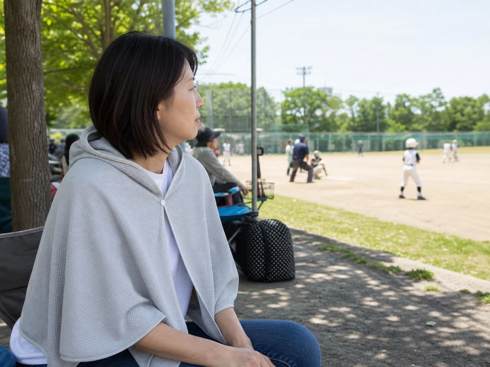 少年野球の観戦中にライトグレーの冷感ポンチョを羽織る保護者