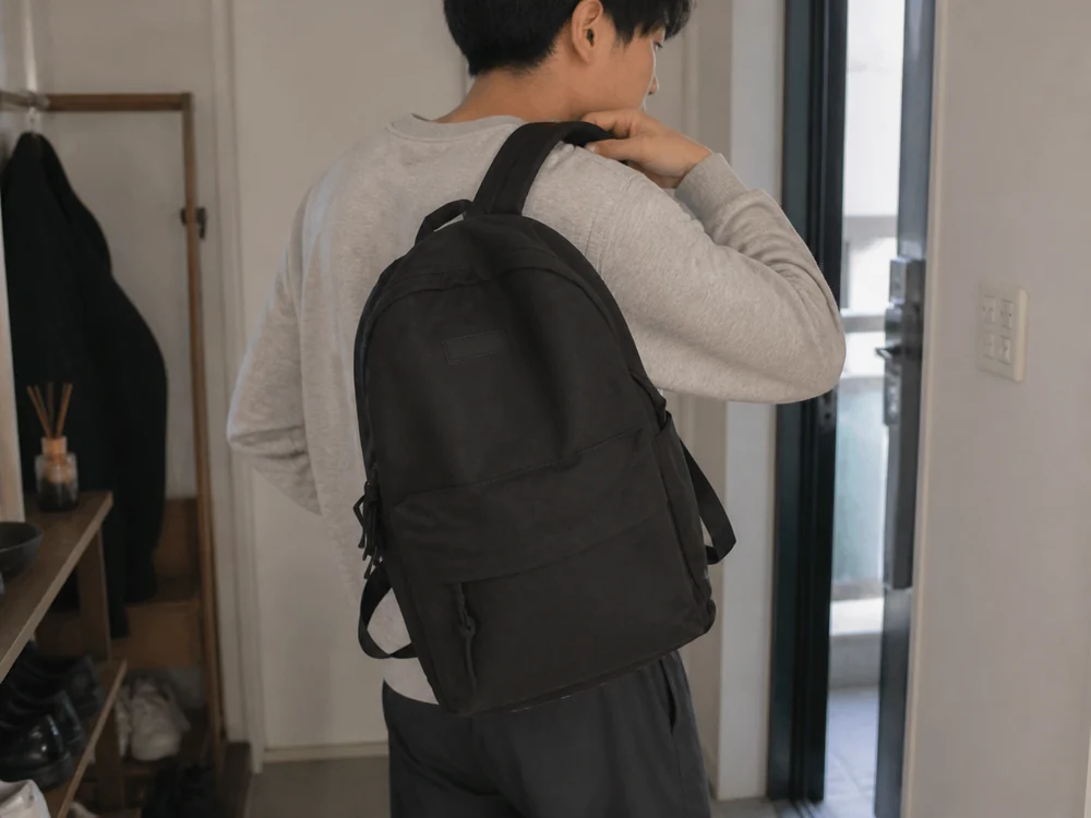 玄関で黒い軽量リュックを背負って出かける通勤者