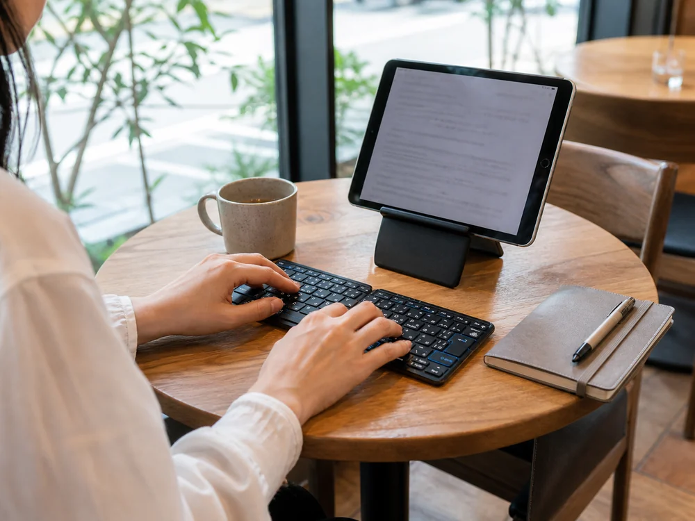 カフェでタブレットと黒い二つ折りキーボードを使って文章を入力する様子