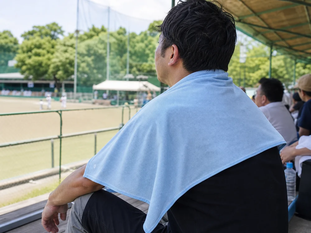 屋外観戦でライトブルーの大判クールタオルを肩に掛ける人